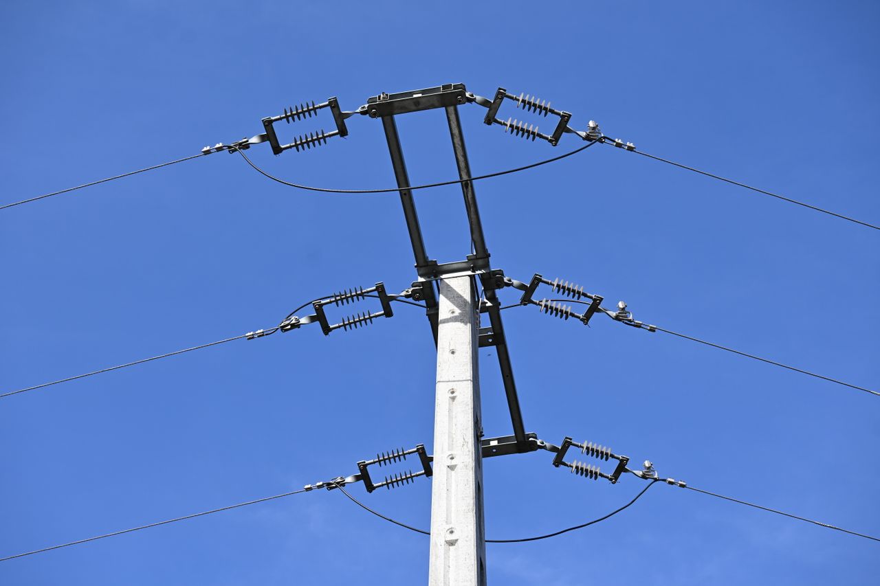 A close-up view of an electricity pole with wires against a clear blue sky, showcasing infrastructure.
